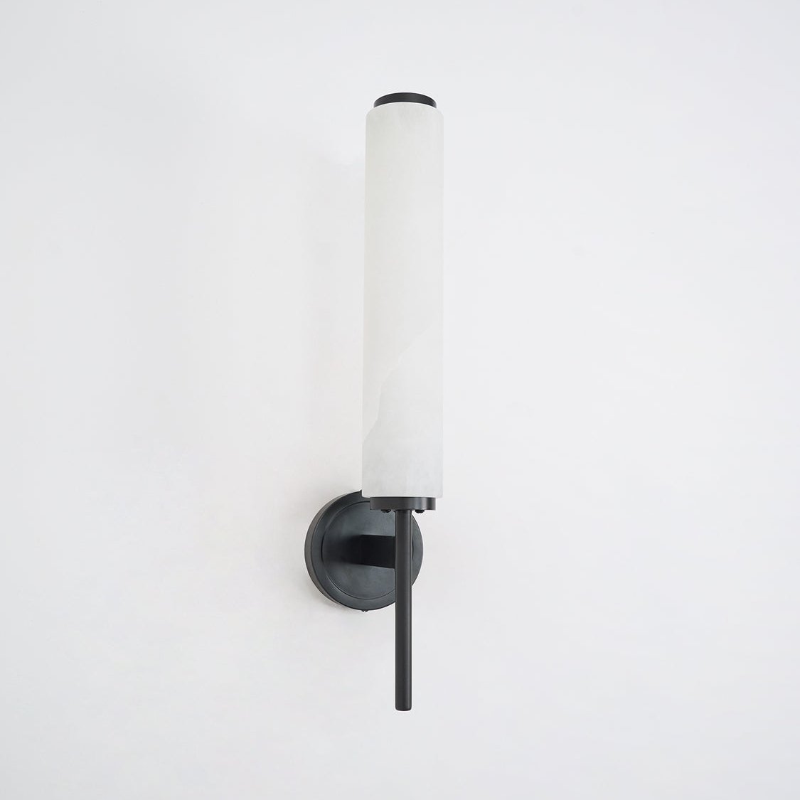 Clérachic Olrinyra in black unlit on a white wall, the alabaster tube cool and pale above the dark mount.