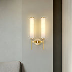The Clérachic Olrinyra twin in brass lit on a pale wall, with a sofa arm just entering the lower frame.