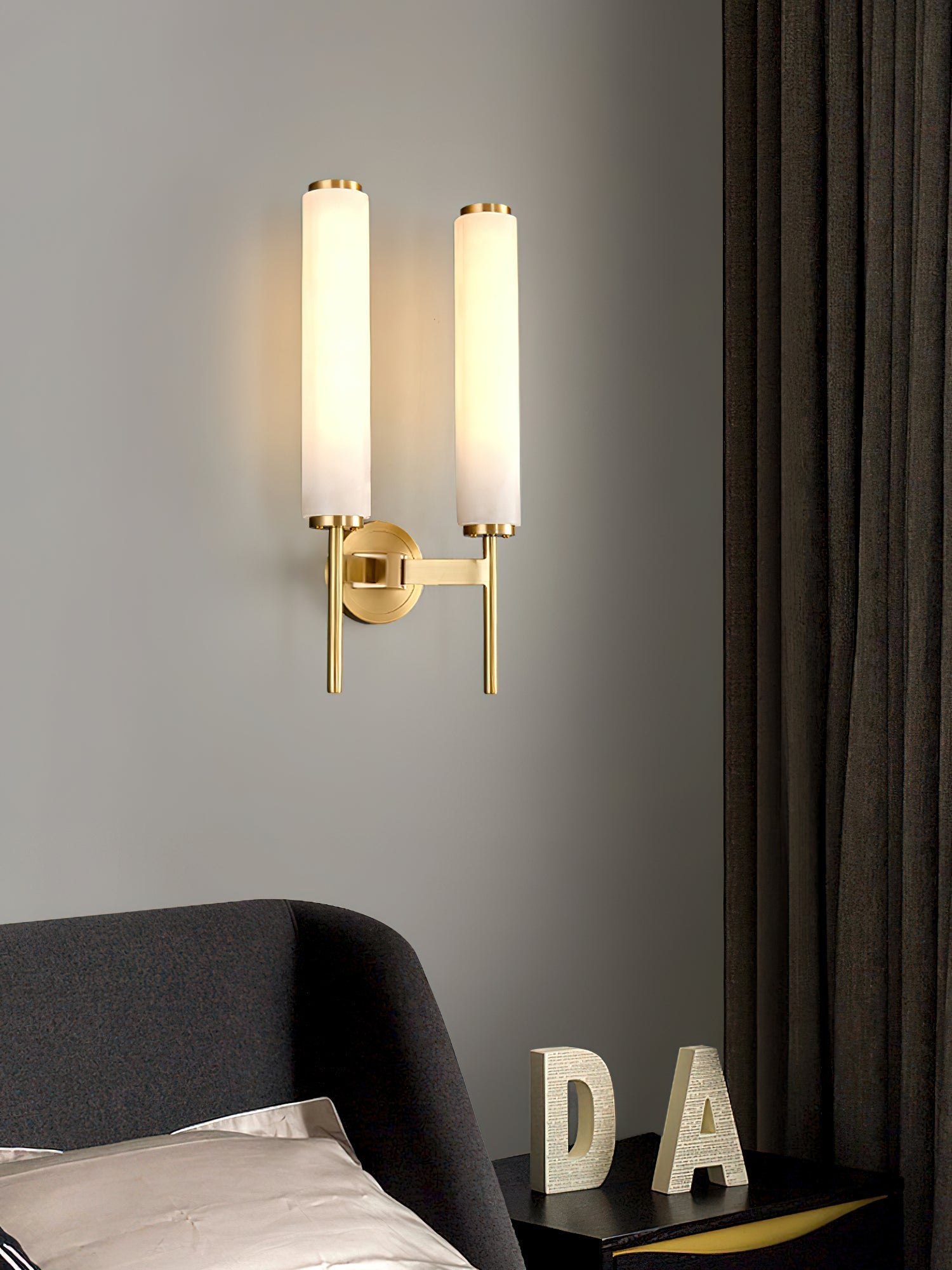 Clérachic Olrinyra twin in brass lit above a bed, beside a nightstand dressed with sculptural letter decor.