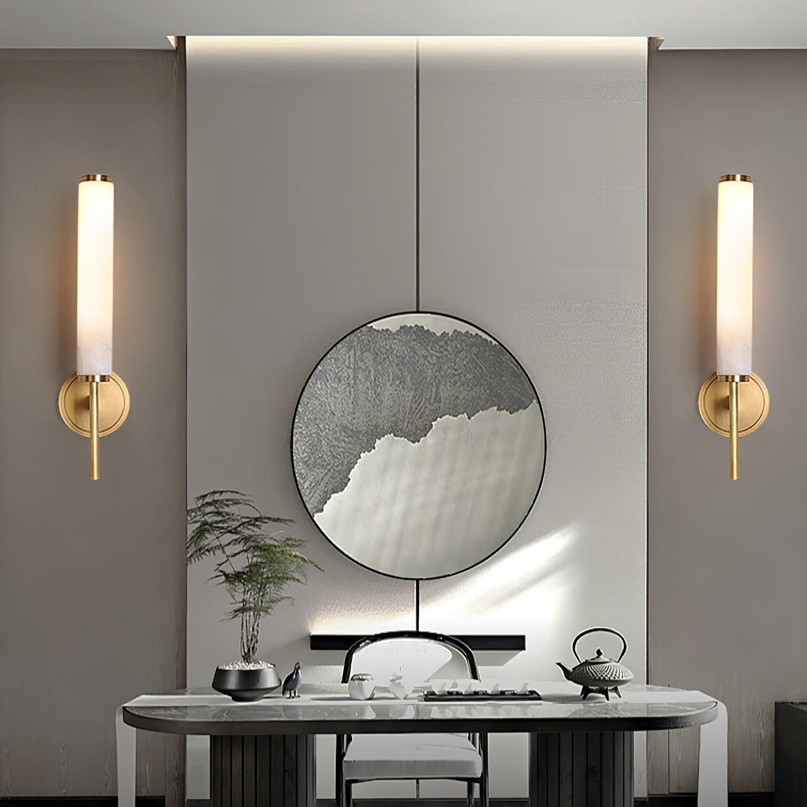 A pair of Clérachic Olrinyra sconces in brass flanking a round mirror above a marble console and tea set.