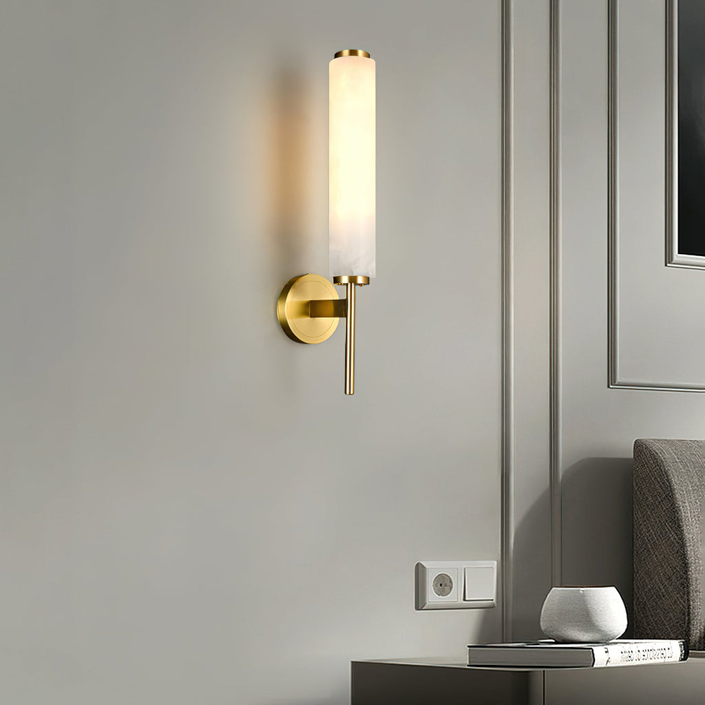 The Clérachic Olrinyra in brass lit beside a wall socket, above a nightstand holding a vase and books.