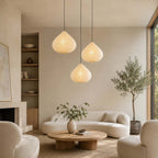 Clérachic onion-shaped paper pendants at staggered heights above a round wooden coffee table in a cream living room, an olive tree by the window.