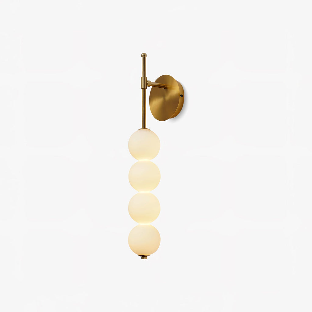 This Clérachic wall light on a plain white backdrop, four glowing opal balls stacked on a slim gold stem with a round gold backplate.