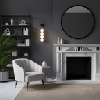 Black-finish Clérachic wall light lit beside a round black mirror in a grey room with a white marble fireplace and a pale armchair.
