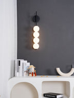 Black-finish Clérachic wall light glowing on a charcoal wall above a white arched console, books and a cream U-shaped ornament.