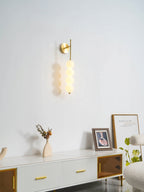 Clérachic wall light in gold with its balls softly lit, above a white sideboard with a framed photo and a vase of dried stems.