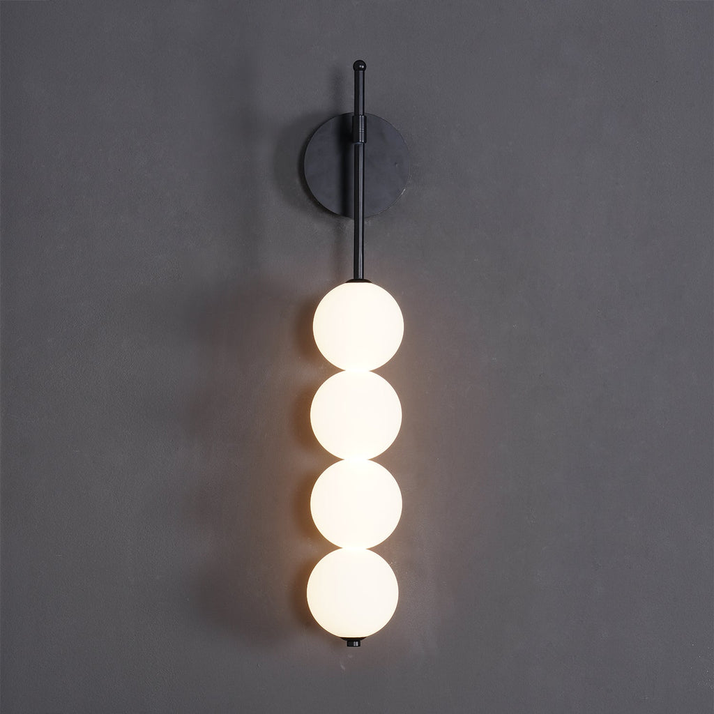 Close front view of the black-finish Clérachic wall light on a charcoal wall, four lit opal balls hanging from a slim black arm.