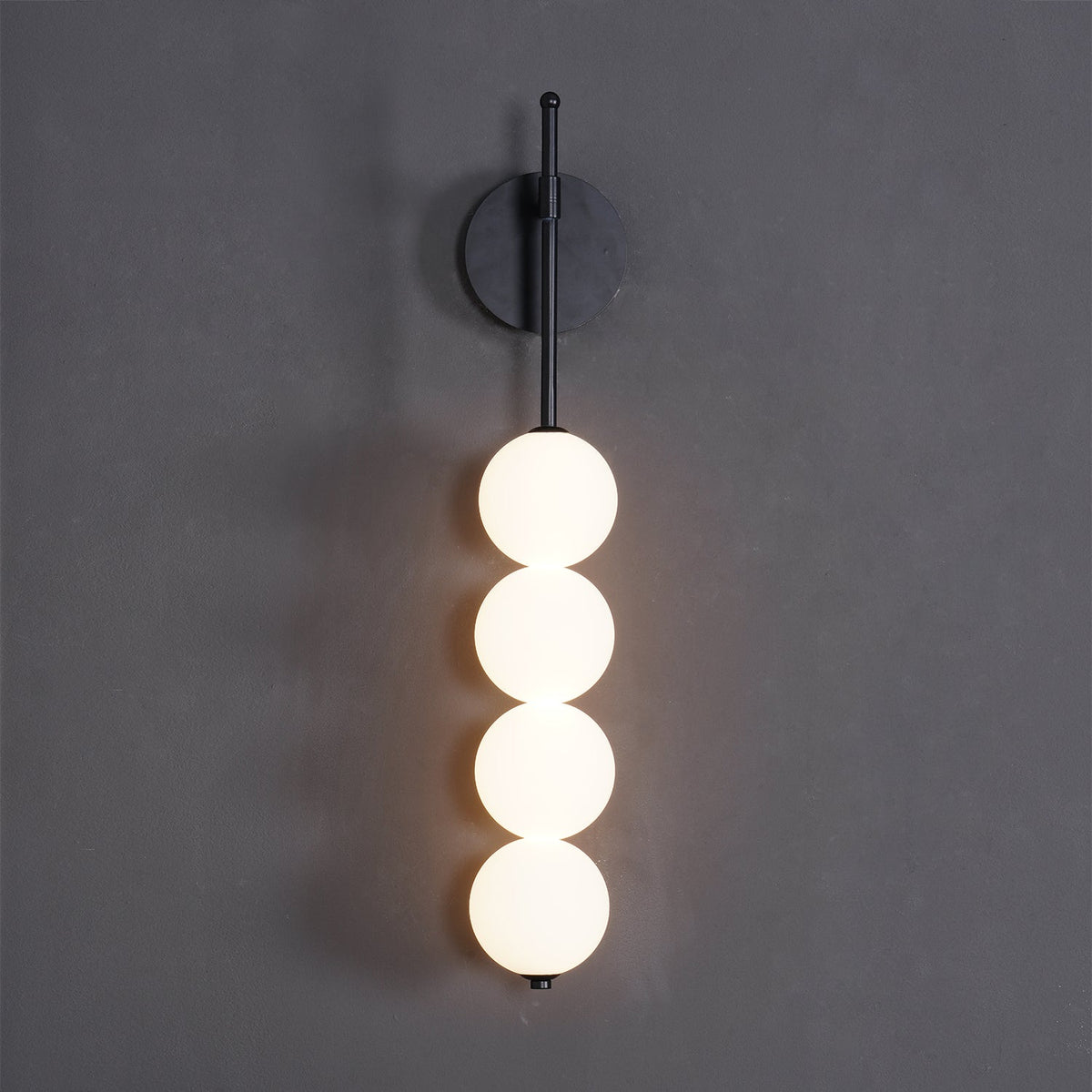 Close front view of the black-finish Clérachic wall light on a charcoal wall, four lit opal balls hanging from a slim black arm.