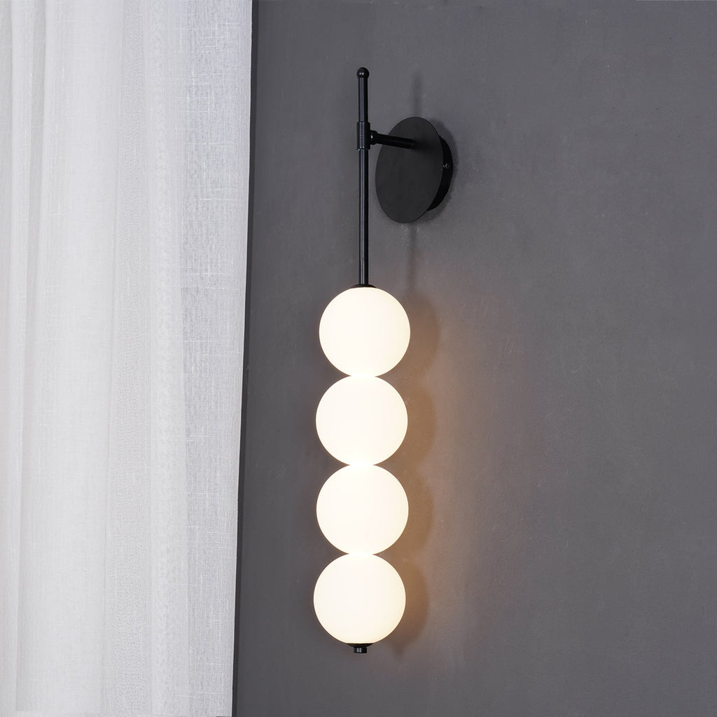 Black-finish Clérachic wall light lit against a grey wall, a white sheer curtain at the left and a warm glow on the wall behind.