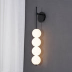 Black-finish Clérachic wall light lit against a grey wall, a white sheer curtain at the left and a warm glow on the wall behind.