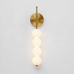 The gold Clérachic wall light lit on a pale grey wall, its four balls glowing a soft warm white.
