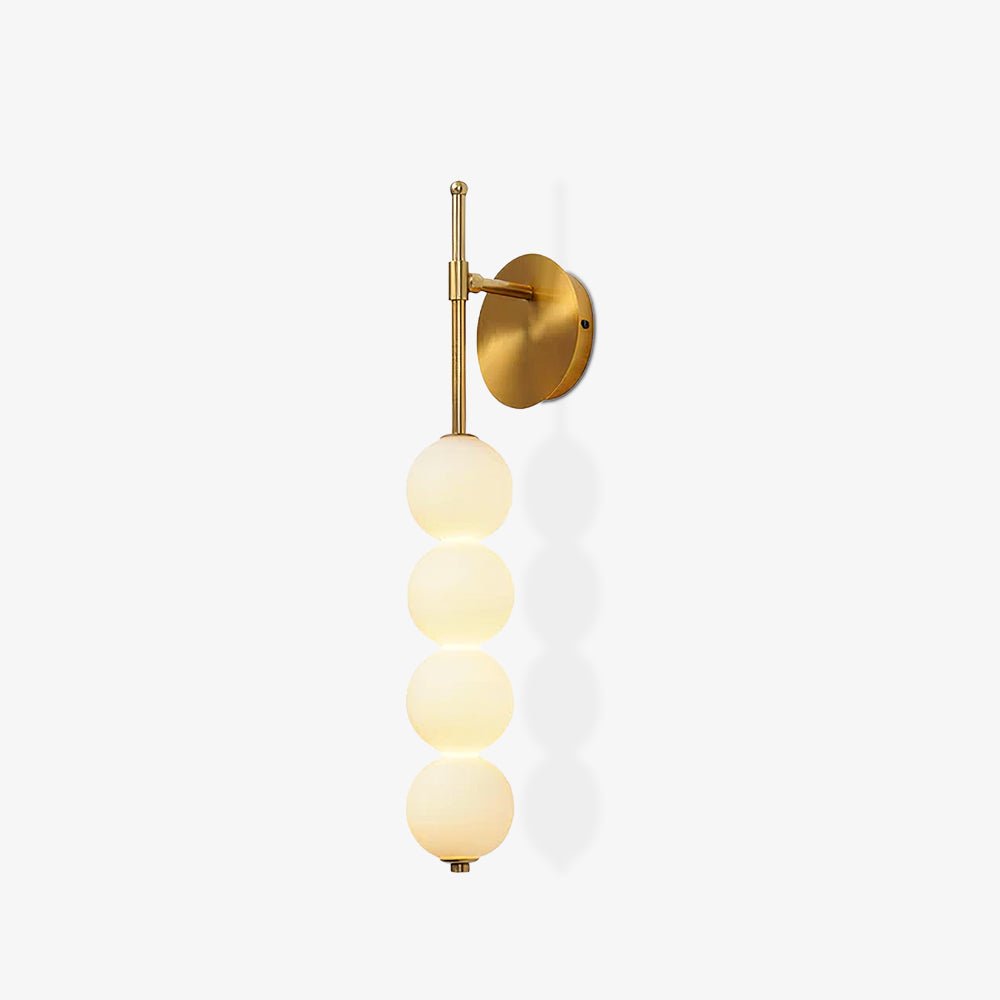 Gold Clérachic wall light lit on a plain white background, seen slightly from the side with the balls' shadows on the wall.