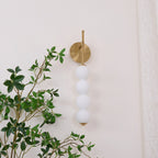 Gold-finish Clérachic wall light, unlit, on a cream wall with a leafy branch behind its four white balls.