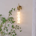 The Clérachic wall light lit in gold, the opal balls glowing warm among green leaves on a pale wall.