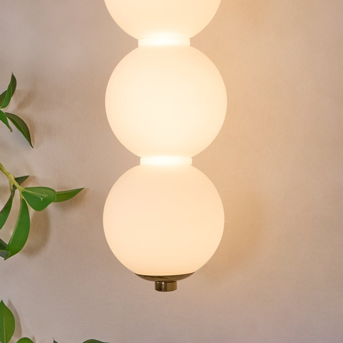 Close view of two glowing opal glass balls and the small brass cap at the base of this Clérachic wall light.
