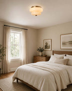A Clérachic flush-mount light on the ceiling of a bedroom with a wooden dresser, a window and a framed print.