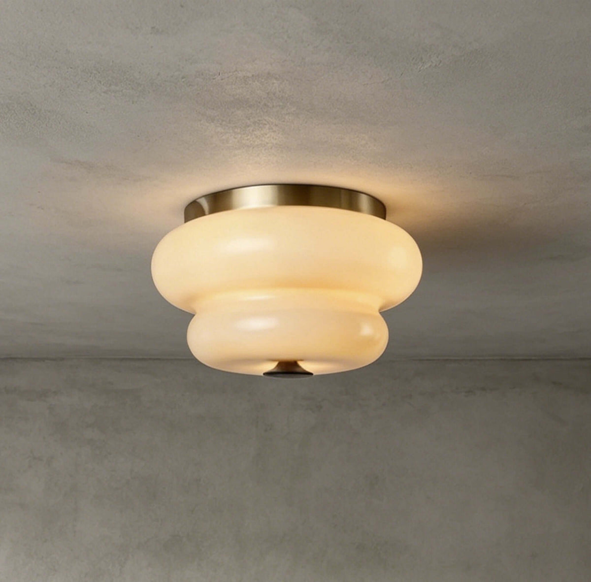 A lit Clérachic flush-mount light with a brass-toned ring, fixed to a rough grey concrete ceiling.