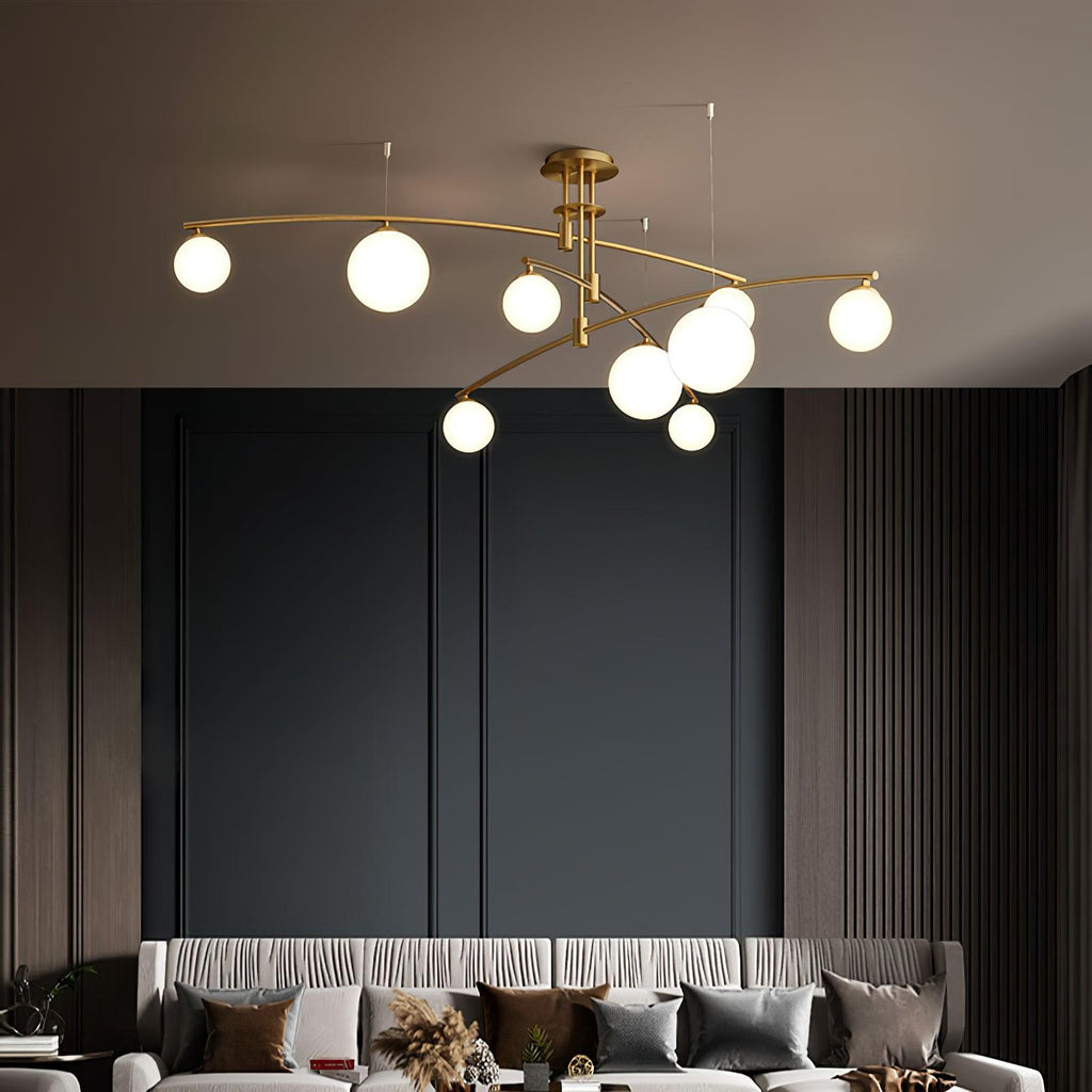Gold Clérachic chandelier with opal globes lit above a sofa with patterned cushions, against dark panelled walls.