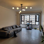 This Clérachic black chandelier glowing a warmer, yellower white in a grey living room with a sofa and a tall window.