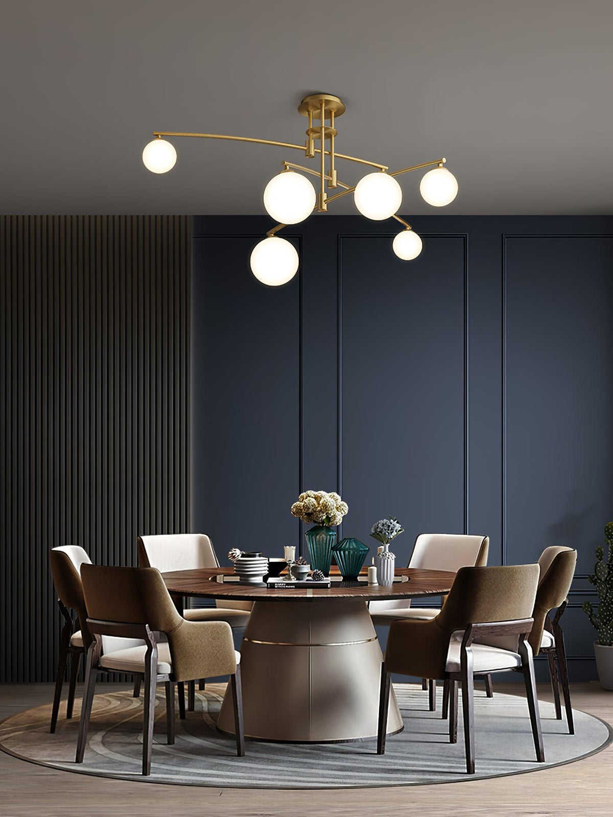 Gold Clérachic chandelier over a round dining table with brown chairs, against a navy panelled wall.