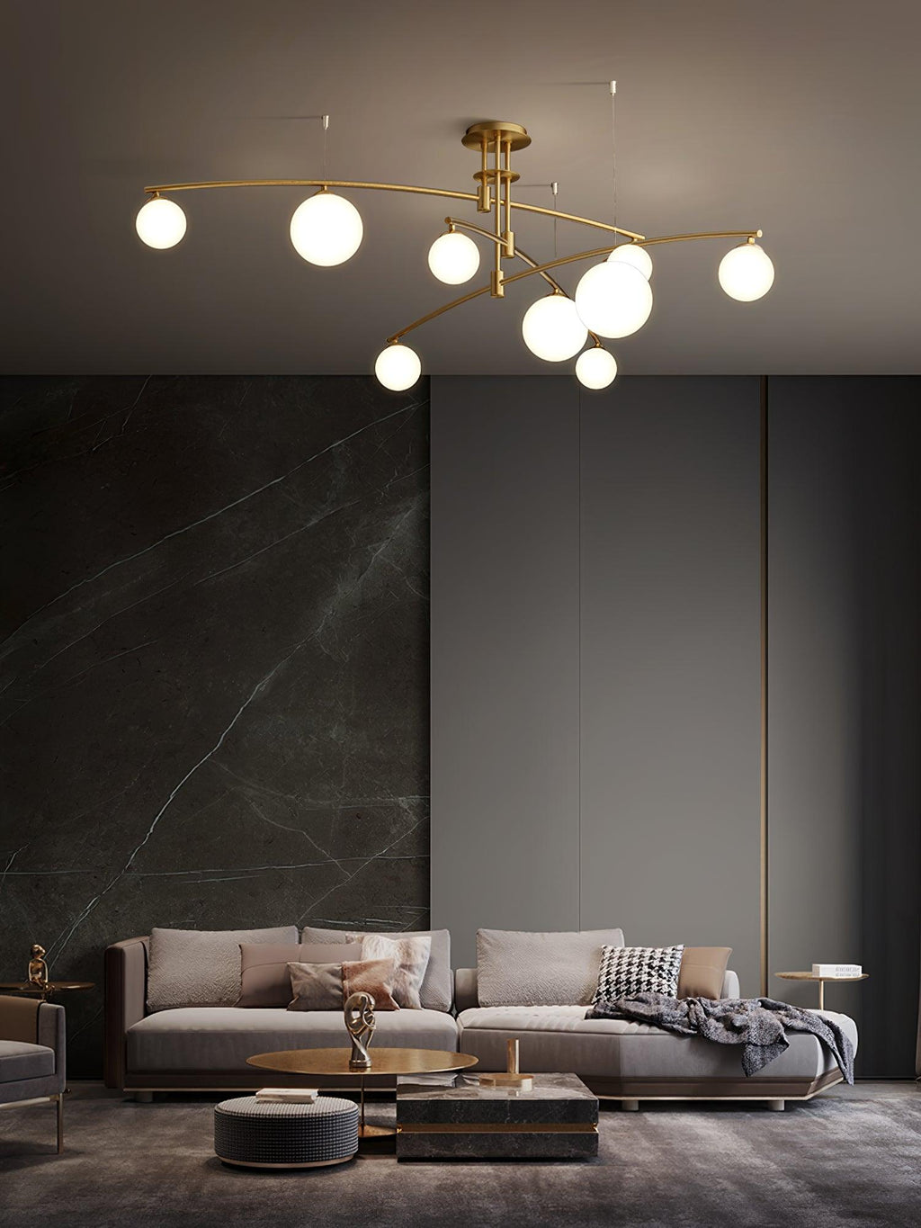 A gold Clérachic chandelier with opal globes over a grey living room with a dark stone feature wall and a low sofa.