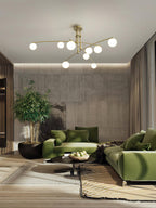 Gold Clérachic chandelier above a living room with green sofas, a concrete-look wall and a large indoor plant.