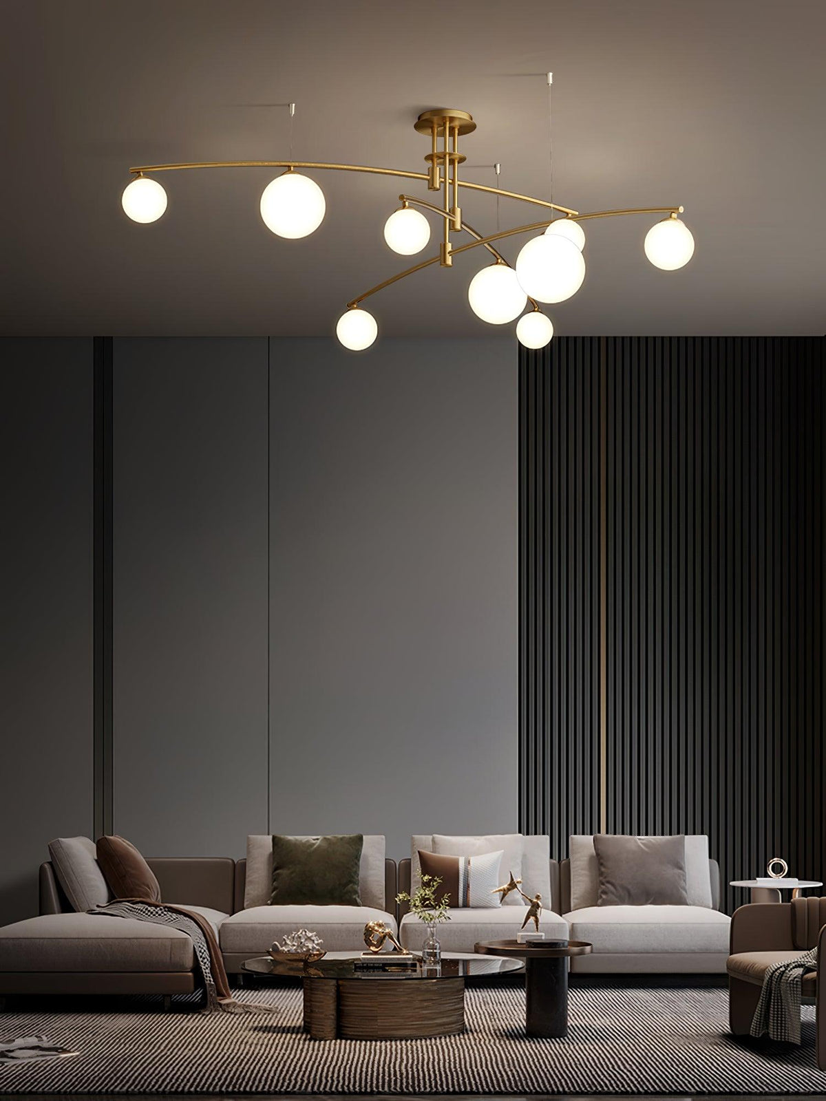 Tall view of a gold Clérachic globe chandelier above a long sofa and round wooden coffee tables in a grey room.