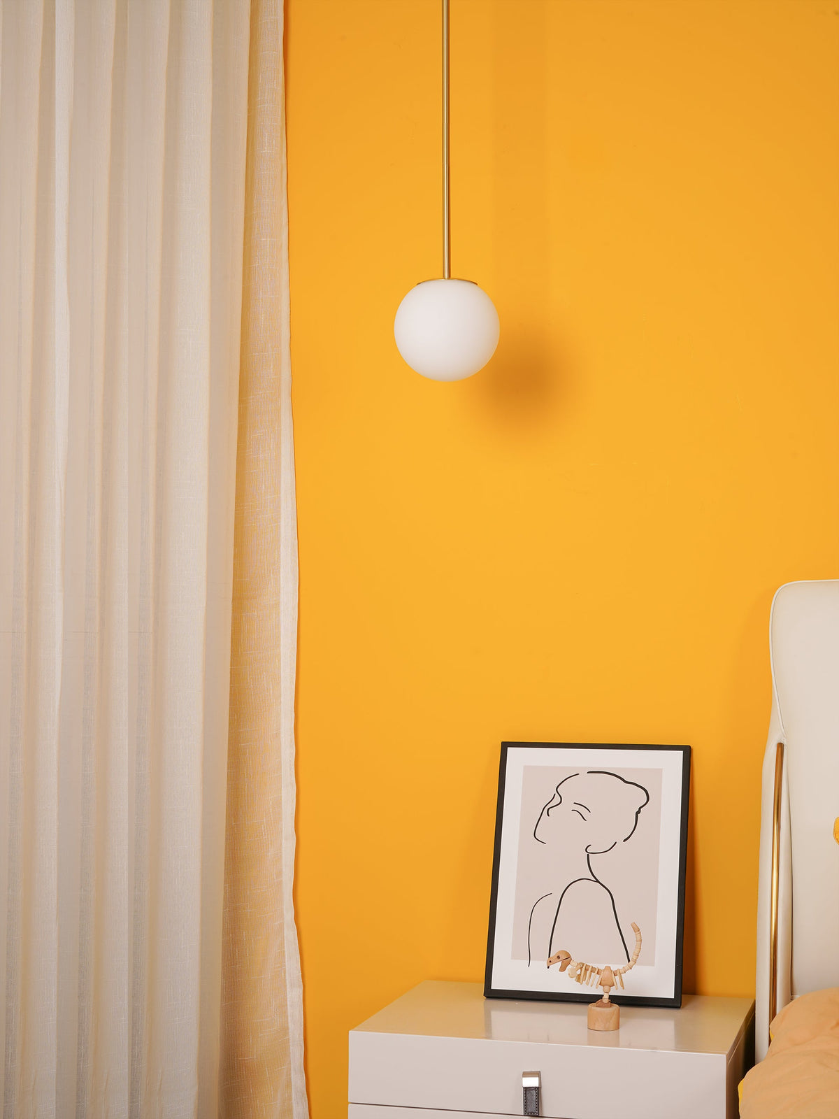 Opal globe on a slim cord against a bright yellow wall, a Clérachic pendant beside cream curtains and a framed line drawing.