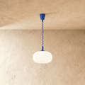 Clérachic pendant with a rounded opal glass shade and a cobalt blue coiled spring cable and canopy, on a plaster wall.