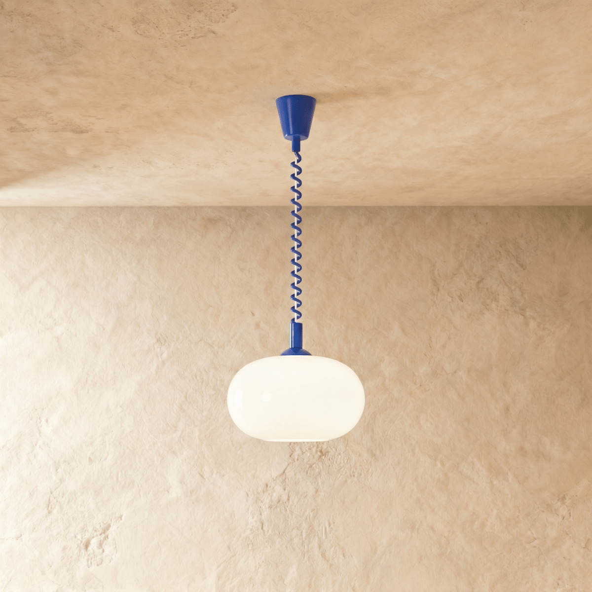 Clérachic pendant with a rounded opal glass shade and a cobalt blue coiled spring cable and canopy, on a plaster wall.