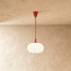 Clérachic pendant with a glowing rounded opal glass shade and a bright red coiled spring cable and canopy on plaster.