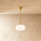 Clérachic pendant with a glowing rounded opal glass shade and an ochre yellow coiled spring cable and canopy.