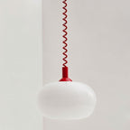 Close view of a Clérachic opal glass pendant shade, white and glossy, with a red coiled spring cable and red cap.
