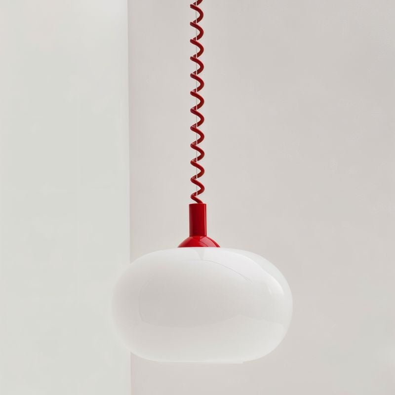 Close view of a Clérachic opal glass pendant shade, white and glossy, with a red coiled spring cable and red cap.