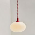 Close view of a Clérachic opal glass pendant lit with a warm cream glow, on a red coiled spring cable and cap.