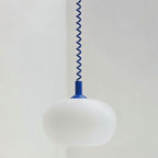 Close view of a Clérachic white opal glass pendant shade with a cobalt blue coiled spring cable and rounded cap.