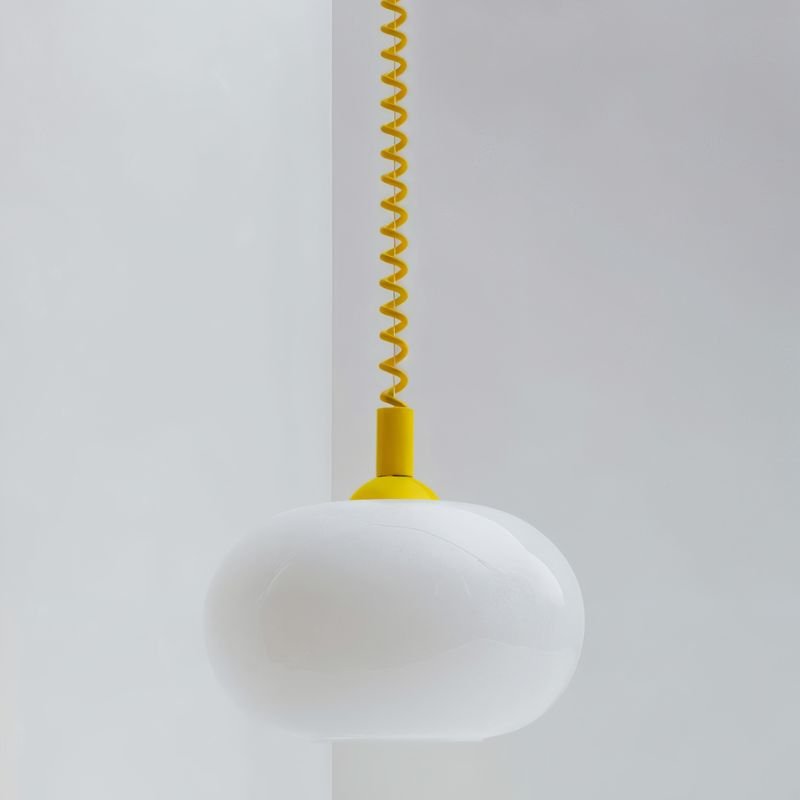 Close view of a Clérachic white opal glass pendant shade with a bright yellow coiled spring cable and rounded cap.
