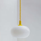 Close view of a Clérachic white opal glass pendant shade with a bright yellow coiled spring cable and rounded cap.