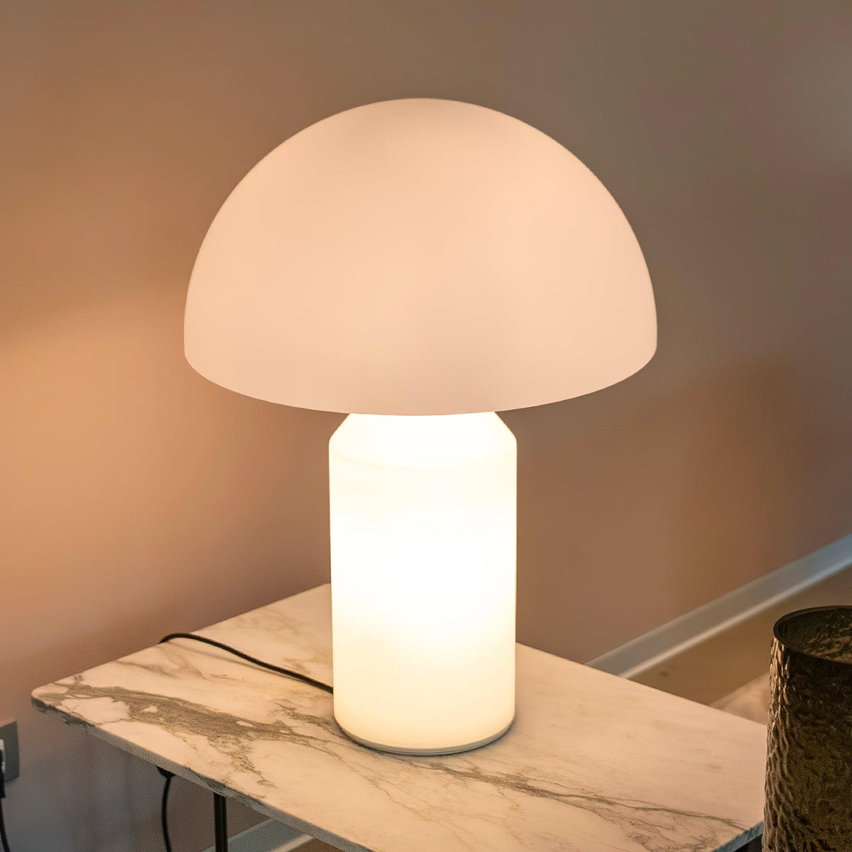 Glowing from within, this Clérachic opal glass table lamp stands on a marble-topped side table against a warm peach wall.