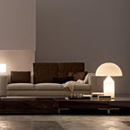 A lit Clérachic opal glass table lamp on a low table in a living room with a beige sofa and dark wood tables.