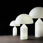 Three Clérachic white glass table lamps in different sizes on a dark background, the dome and cone-topped cylinder shape clear.