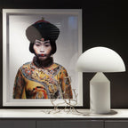 A Clérachic white glass table lamp beside a large framed portrait and a silver branch sculpture on a white sideboard.