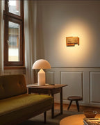 In a quiet corner with an olive-green sofa, a Clérachic white glass table lamp glows on a wooden side table beside a stool.