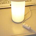 Close view of the cylinder base of this Clérachic table lamp lit from within, with its white cord and in-line switch alongside.