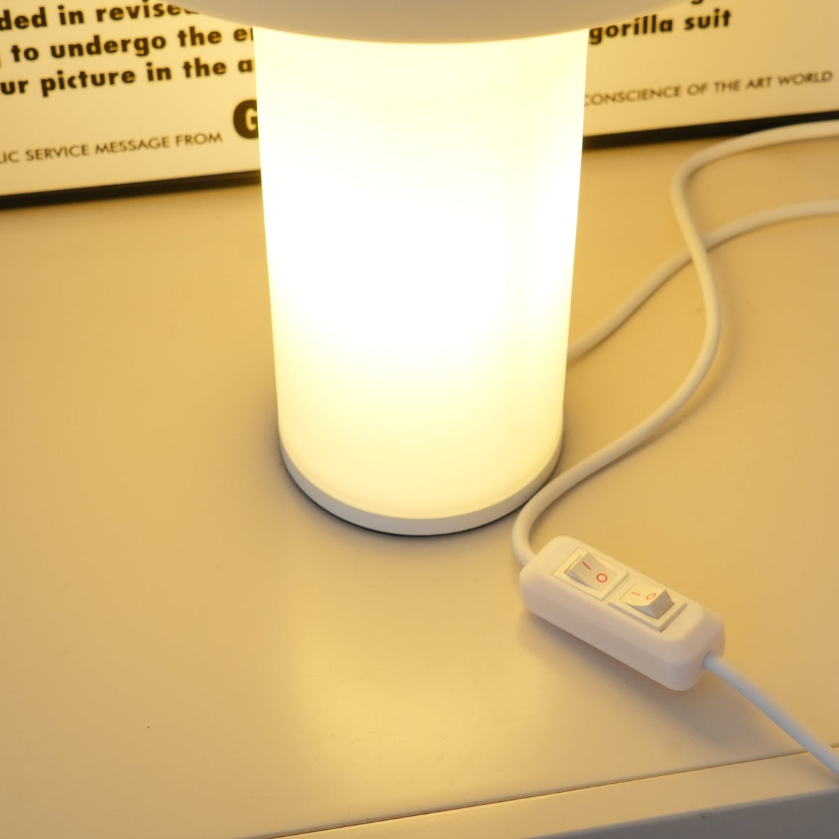 Close view of the cylinder base of this Clérachic table lamp lit from within, with its white cord and in-line switch alongside.