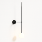 Clérachic black wall light switched on, its opal glass globe glowing softly at the foot of a long slim rod.