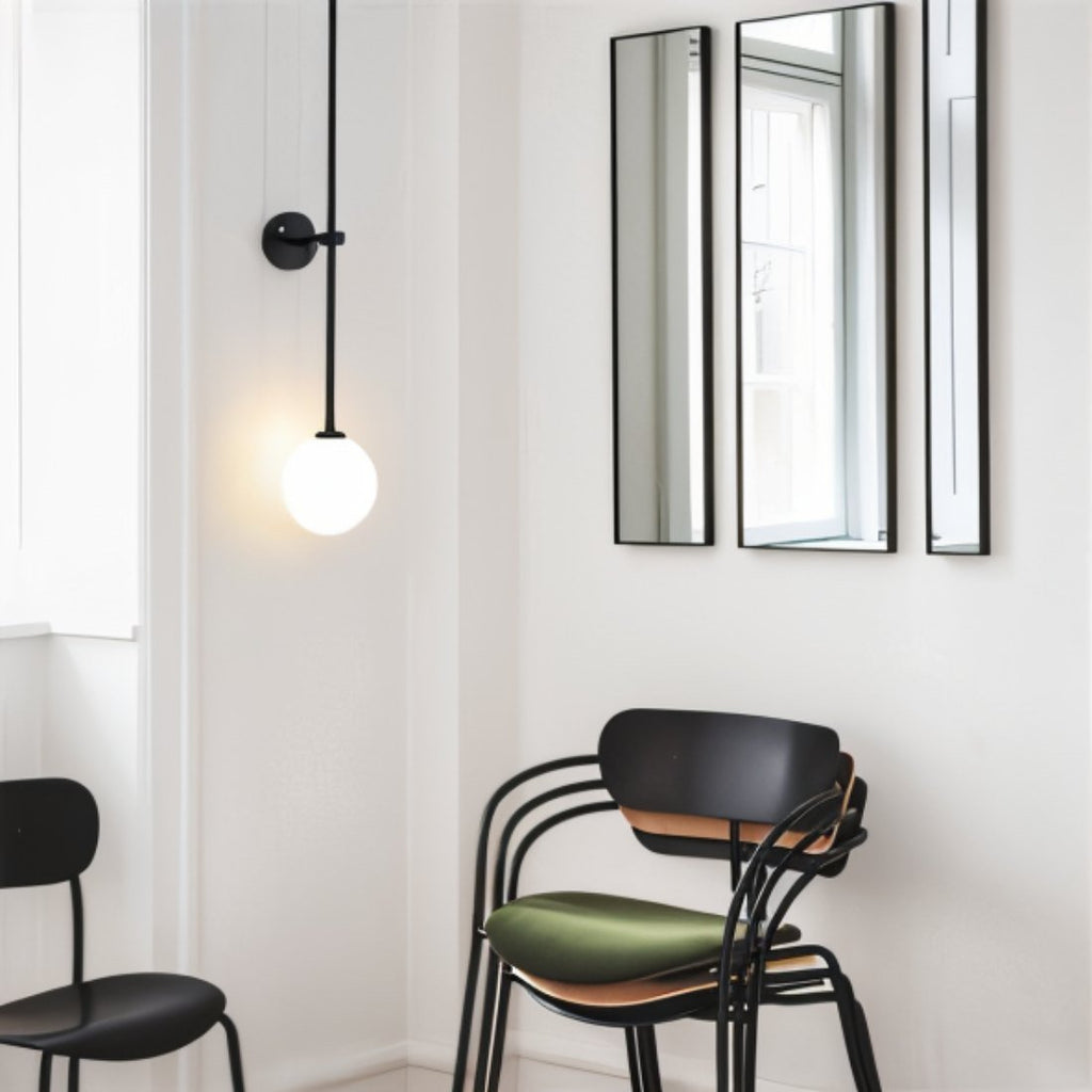 Clérachic black wall light with a lit opal globe in a white room with slim mirrors and black chairs.