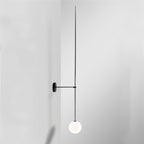 Clérachic black wall light with an extra-long slim rod and a white opal glass globe in a pale grey corner.