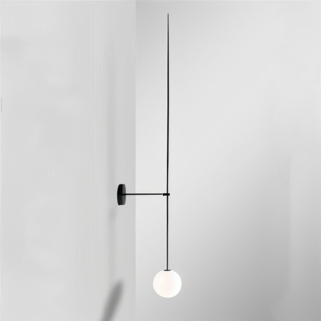Clérachic black wall light with an extra-long slim rod and a white opal glass globe in a pale grey corner.