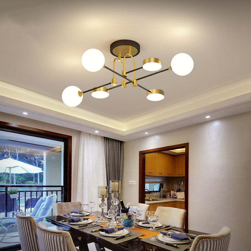 Overhead view of the Clérachic Opal Globe Ceiling Light's black-and-gold crossed arms lighting a dining table set for a meal.